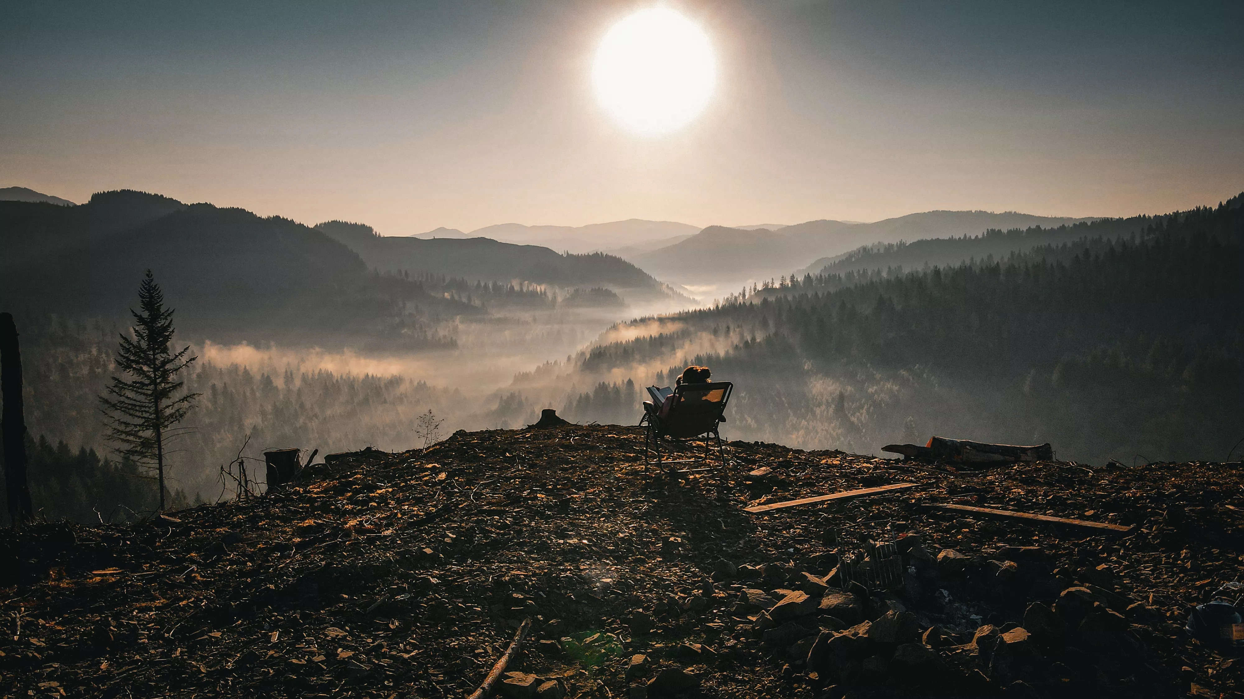 A person sitting in a camp chair overlooking a fog-filled valley at sunrise